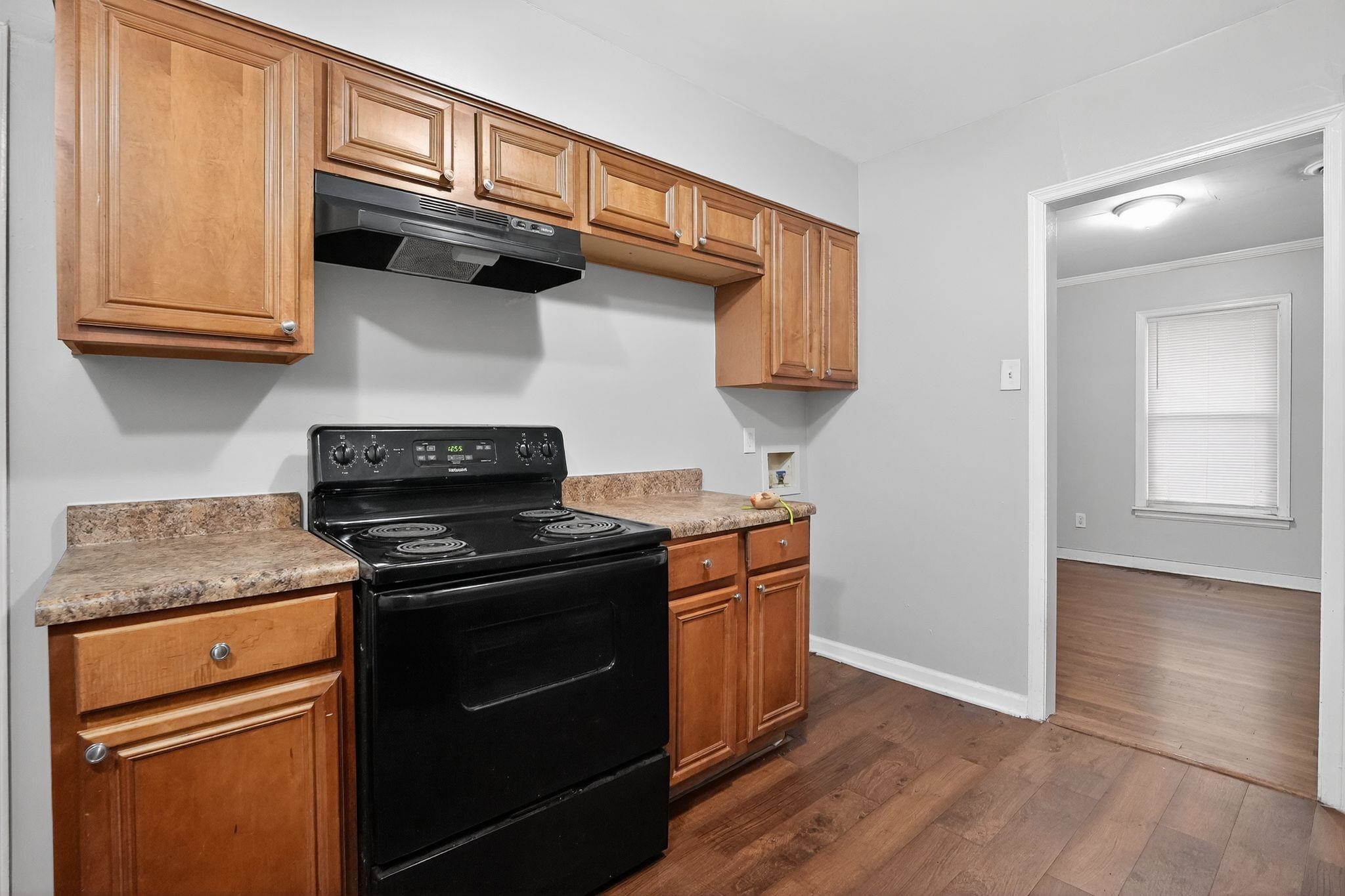 177 East Raines Road Memphis, TN 38109 - Photo 15 of 32 Kitchen featuring black electric range, under cabinet range hood, dark wood-type flooring, brown cabinetry, and light countertops