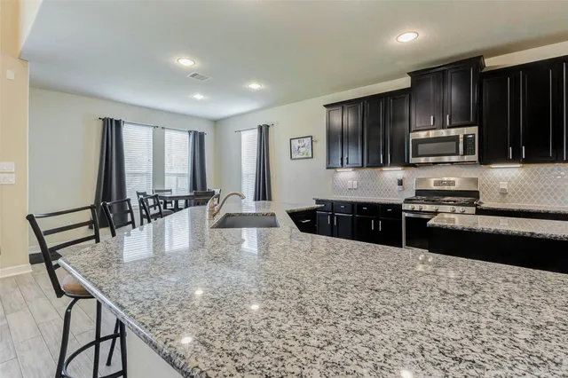 a kitchen with kitchen island granite countertop a stove a sink a microwave a dining table and chairs