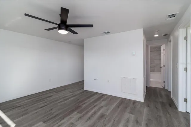 an empty room with wooden floor fan and windows