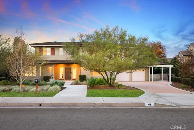 a view of a white house with a small yard and large trees