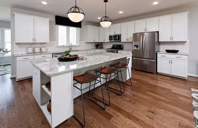 a kitchen with stainless steel appliances granite countertop a stove a refrigerator a sink a stove and white cabinets with wooden floor