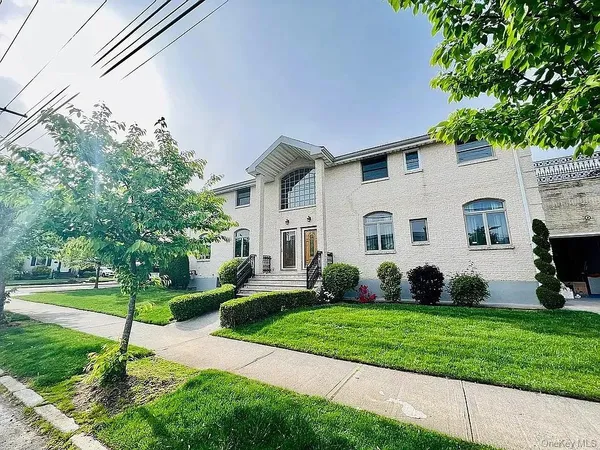 a view of a white house in front of a yard with plants and large trees