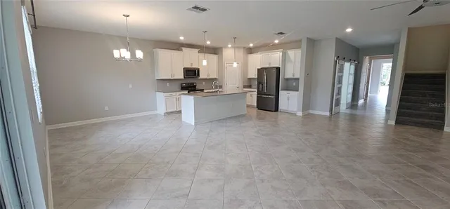 a view of an empty room with kitchen and window