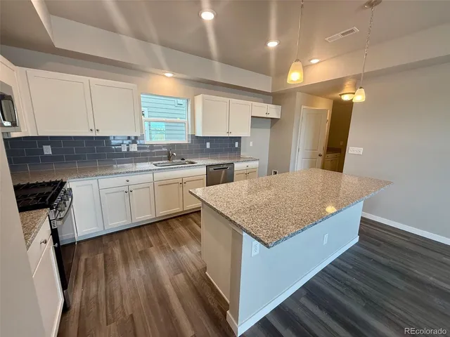 a kitchen with a sink dishwasher a stove and white cabinets with wooden floor