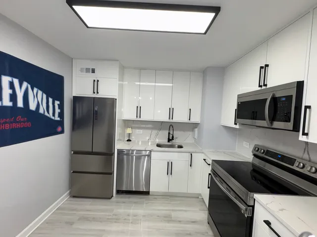 a kitchen with stainless steel appliances a white stove top oven a sink and dishwasher a refrigerator with white cabinets