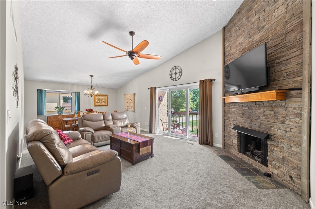 889 Hampton Ridge Drive Akron, OH 44313 - Photo 10 of 38 Living room featuring ceiling fan with notable chandelier, carpet, high vaulted ceiling, and a stone fireplace