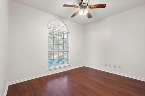 an empty room with wooden floor chandelier fan and windows