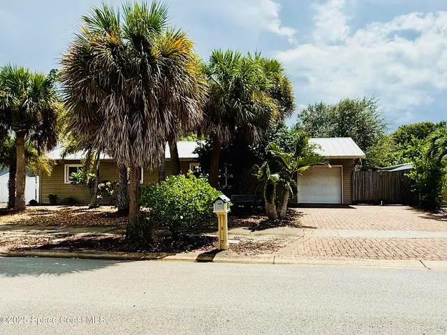 a view of a white house with a yard plants and palm trees