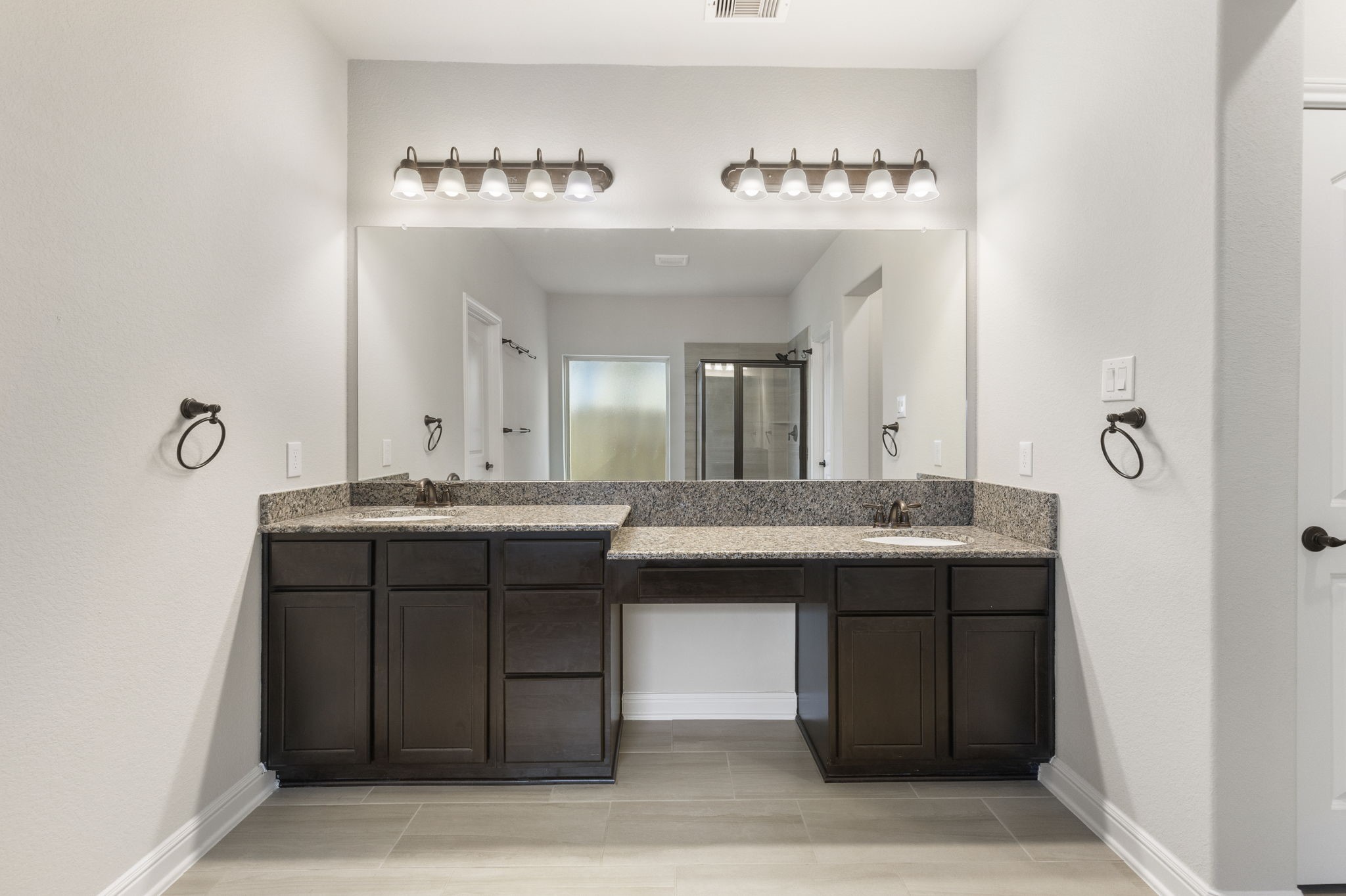 2819 Bradbury Hills Road Spring, TX 77373 - Photo 34 of 50 This photo features a modern bathroom with dual sinks and dark wood cabinetry, granite countertops, and a large mirror with overhead lighting. The space is bright with neutral wall colors and tile flooring.