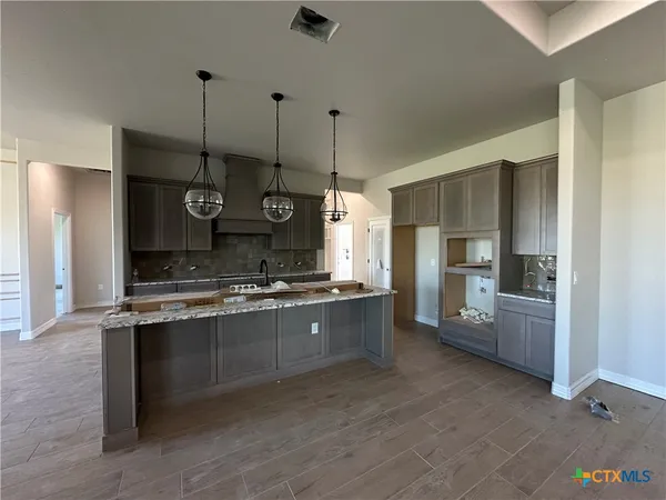 a large kitchen with granite countertop a stove a sink dishwasher a refrigerator and a wooden floor