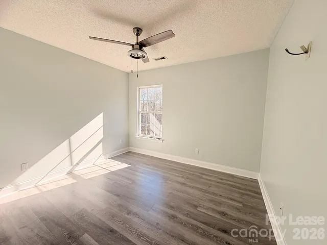 an empty room with wooden floor fan and windows