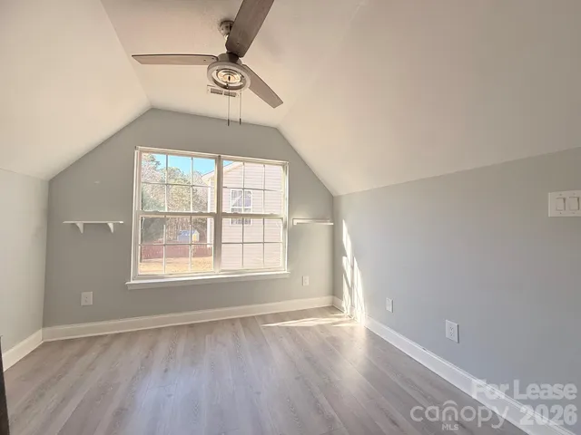 an empty room with wooden floor windows and fan