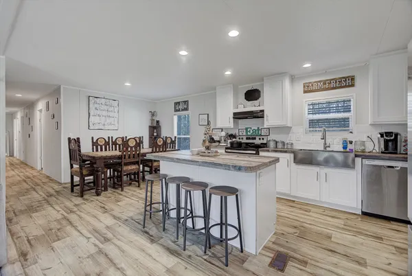 a kitchen with stainless steel appliances granite countertop a stove a sink a refrigerator a dining table and chairs with wooden floor