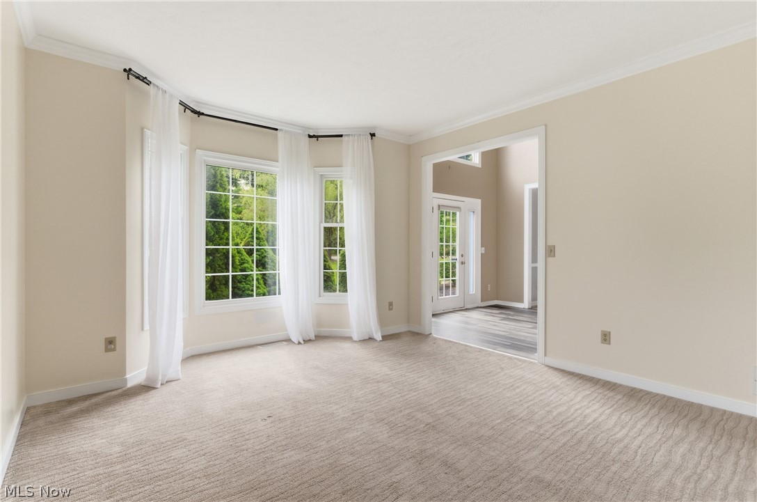 11678 Dunham Road Northfield, OH 44067 - Photo 11 of 38 Living space featuring a curved bay window with grid-patterned panes, light-toned carpeting, crown molding, and an open doorway leading to an area with wood-finish flooring and double French doors