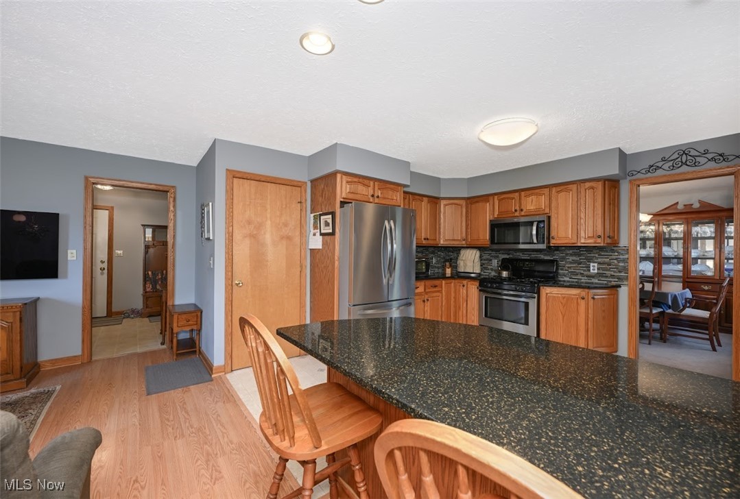 3305 Edington Road Akron, OH 44333 - Photo 14 of 46 Kitchen featuring stainless steel appliances, light wood-style floors, a kitchen breakfast bar, brown cabinets, and backsplash