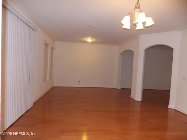 a view of an empty room with chandelier fan and wooden floor