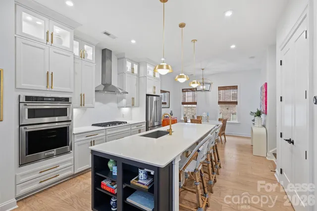 a kitchen with stainless steel appliances kitchen island granite countertop a stove a refrigerator a kitchen island a dining table and chairs with wooden floor