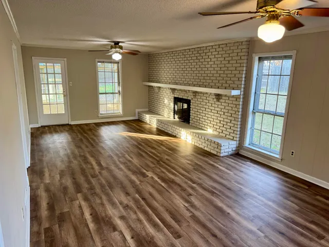 an empty room with wooden floor fireplace and windows