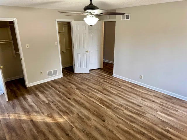 a view of an empty room with wooden floor and a ceiling fan