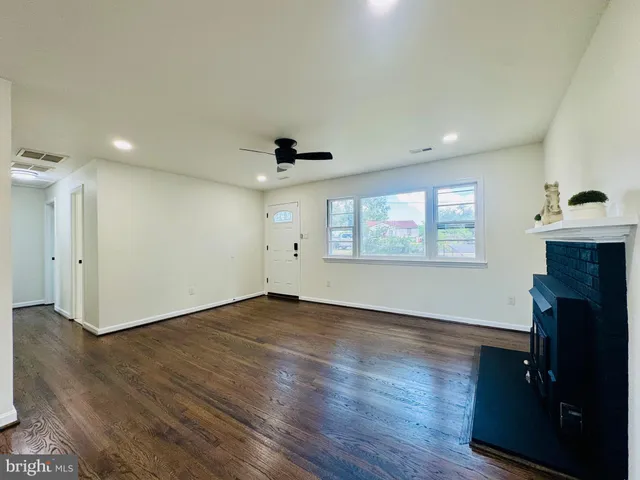 an empty room with wooden floor a ceiling fan a fireplace and windows