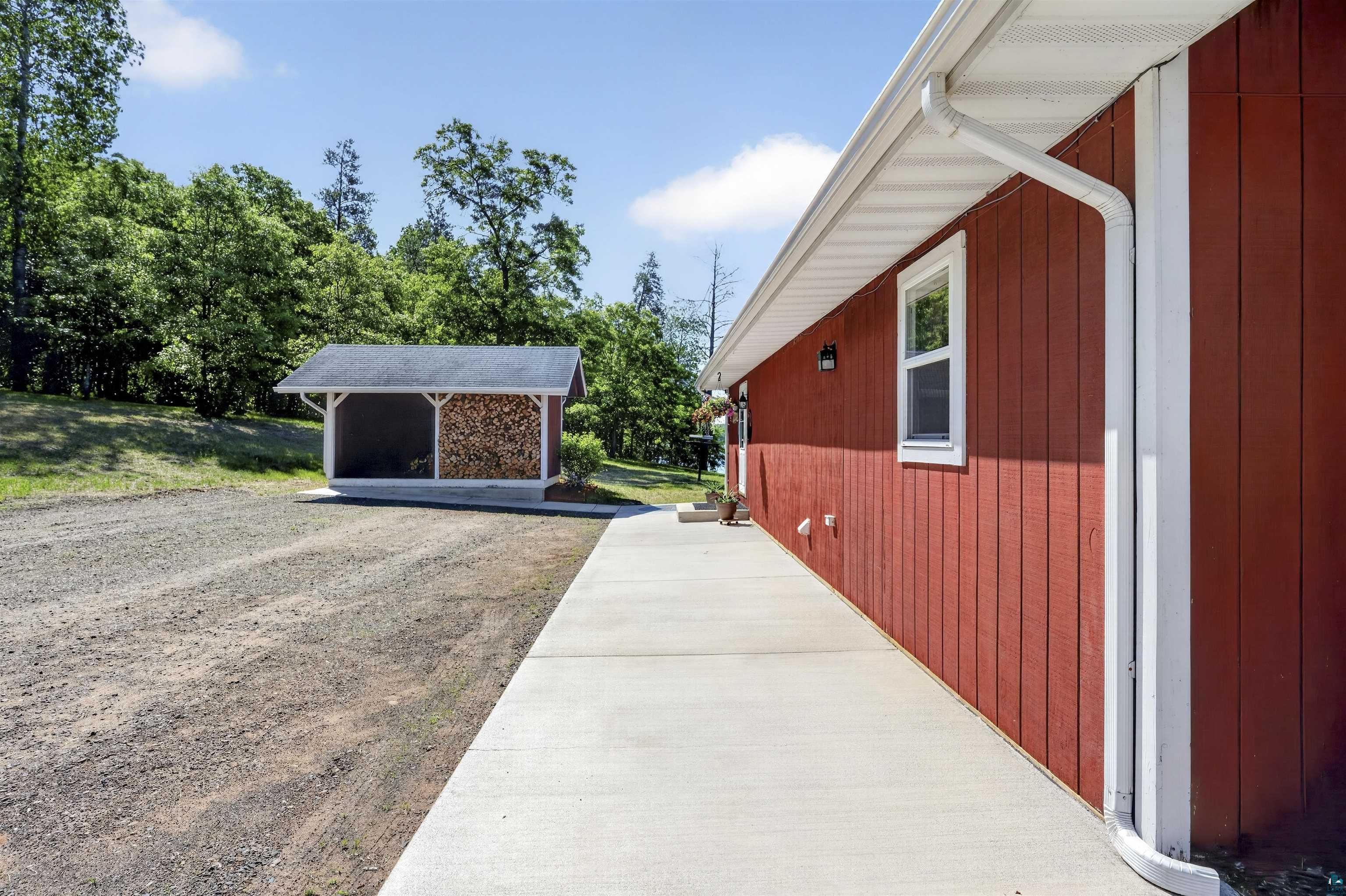 11702 East Mail Road Gordon, WI 54838 - Photo 32 of 60 Red vertical plank siding with white trim and gutters, complemented by a concrete walkway
