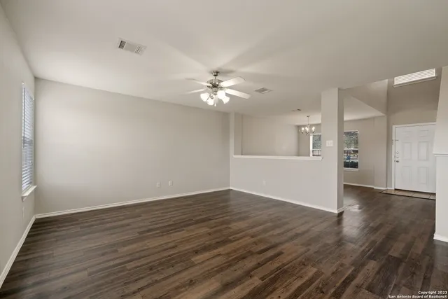 a view of an empty room with wooden floor and a ceiling fan