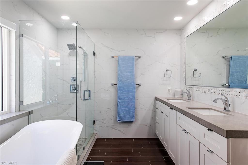 748 Reef Point Circle Naples, FL 34108 - Photo 14 of 23 Full bath featuring tile walls, a soaking tub, double vanity, a marble finish shower, and wood tiled floors