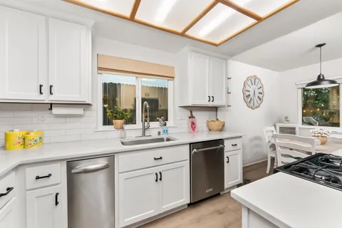 a kitchen with a sink dishwasher and white cabinets with wooden floor