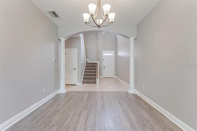 an empty room with wooden floor chandelier fan and windows