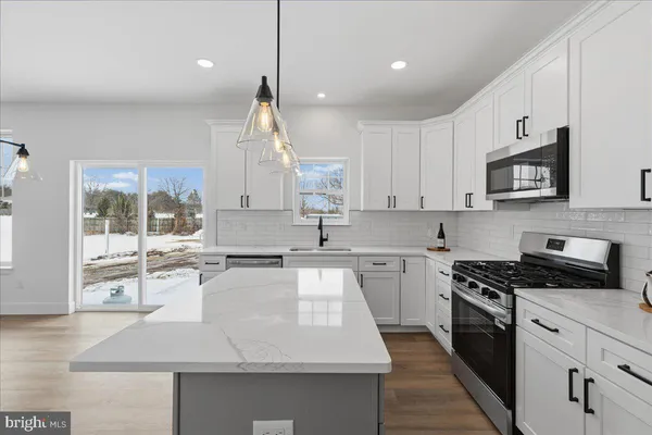 a large kitchen with granite countertop a stove a sink a refrigerator and white cabinets with wooden floor