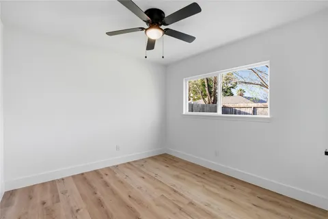 an empty room with wooden floor ceiling fan and window