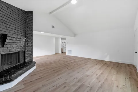 a view of an empty room with wooden floor fireplace and a window