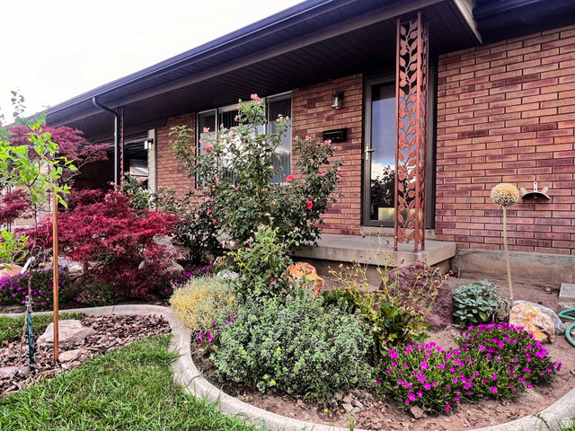 8097 South 535 East Sandy, UT 84070 - Photo 13 of 15 Brick exterior with a decorative metal column, concrete entry, and established landscaping featuring various plantings and a Japanese maple
