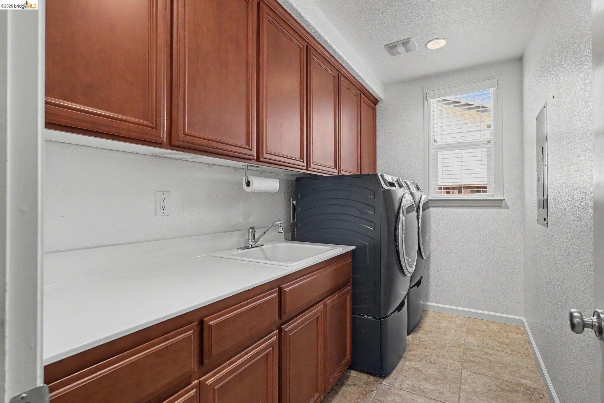 106 Little Ranch Circle Oakley, CA 94561 - Photo 10 of 34 Laundry room featuring wood-finish cabinetry, a white countertop, and an integrated sink with a chrome faucet