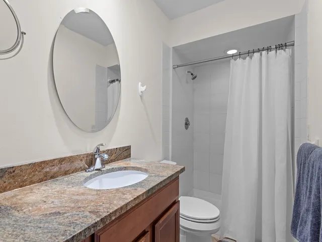 a bathroom with a granite countertop sink toilet a mirror and shower curtain