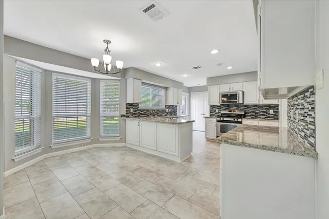 a large kitchen with granite countertop a stove a sink a refrigerator and white cabinets with wooden floor