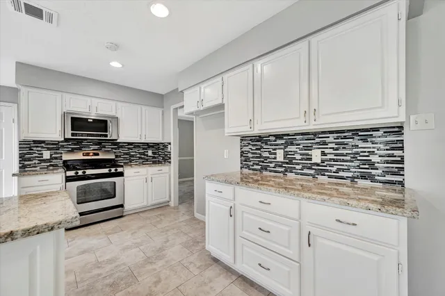a kitchen with granite countertop white cabinets and stainless steel appliances