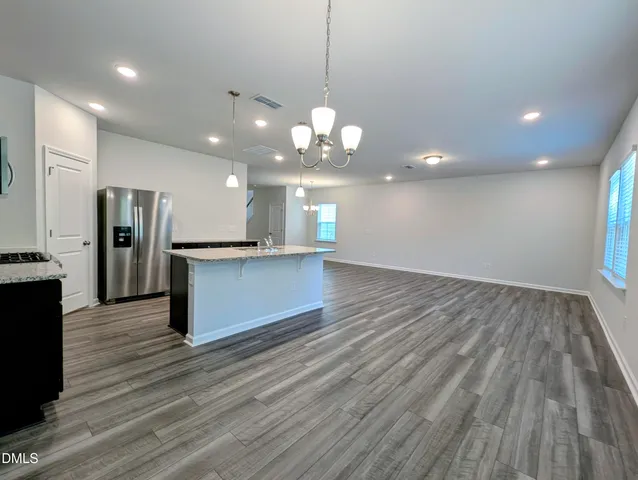 a view of an empty room with wooden floor and a kitchen