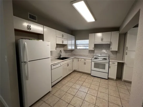 a white kitchen with sink a refrigerator and white cabinets