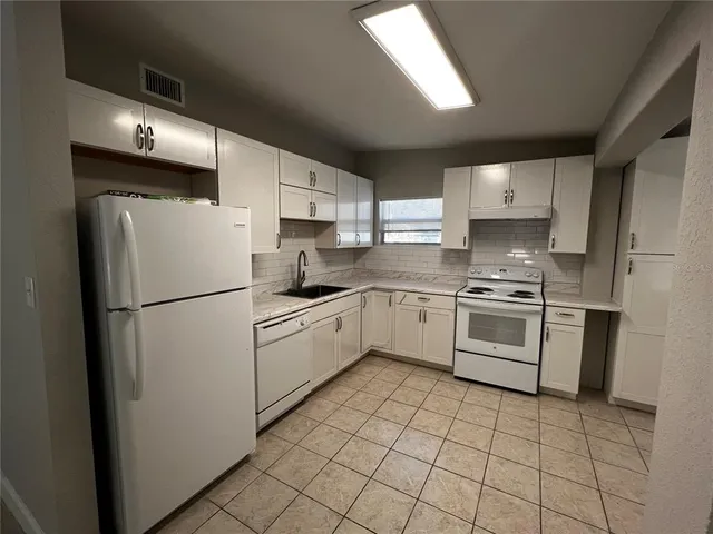 a white kitchen with sink a refrigerator and white cabinets