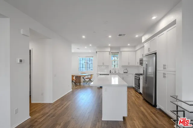 a living room with stainless steel appliances furniture refrigerator and wooden floor