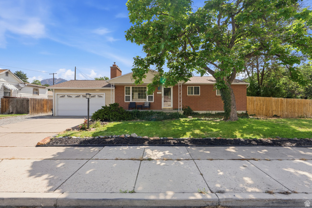 7795 South 1000 East Midvale, UT 84047 - Photo 2 of 42 Brick exterior with white trim, featuring a front lawn with mature trees and a concrete driveway