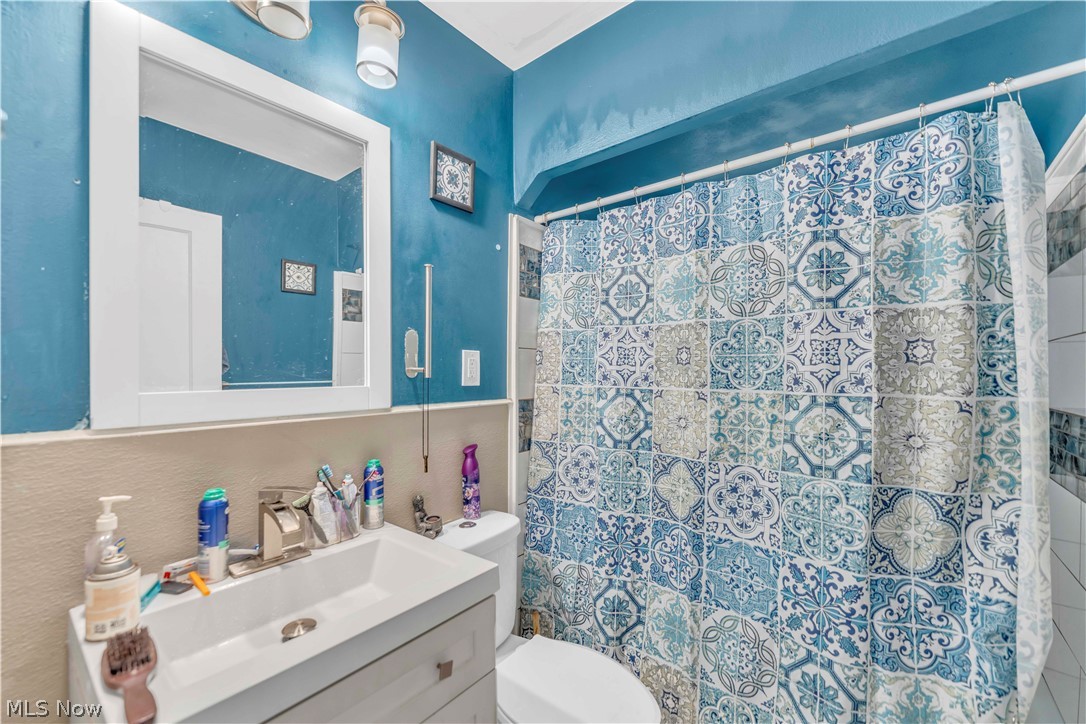 3731 Lowell Road Cleveland Heights, OH 44121 - Photo 11 of 29 Spa-inspired bathroom featuring vibrant turquoise walls, a large framed mirror above a white vanity sink, and an ornate blue and white patterned tile shower surround with glass enclosure