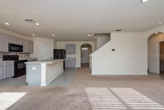 a large white kitchen with stainless steel appliances kitchen island granite countertop a refrigerator and a stove top oven