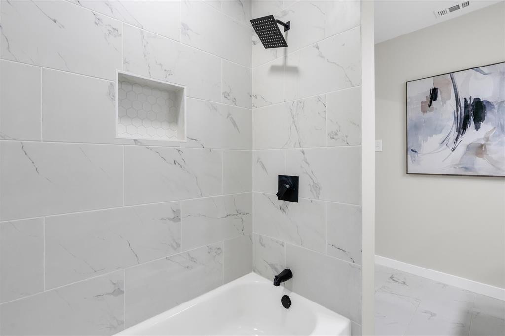 4815 Kelman Street Dallas, TX 75214 - Photo 30 of 37 Bathtub and shower combination featuring large format marble-look wall tiles, a built-in shower niche with honeycomb tile inlay, and matte black fixtures including a rainfall showerhead