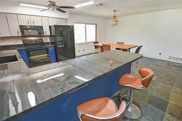 a kitchen with stainless steel appliances granite countertop a sink a stove a refrigerator cabinets and chairs