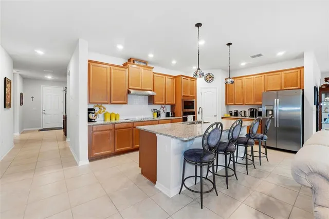 a kitchen with stainless steel appliances kitchen island granite countertop a refrigerator oven a sink a dining table and chairs with wooden floor