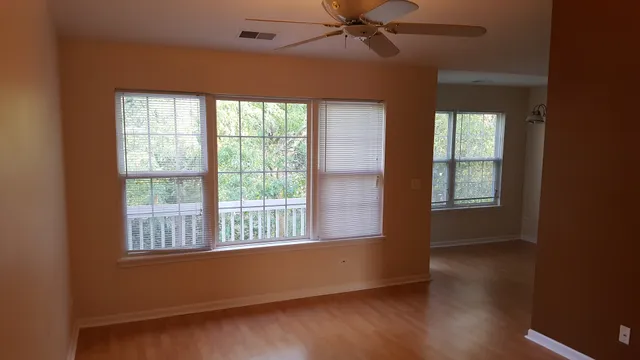 an empty room with wooden floor fan and windows
