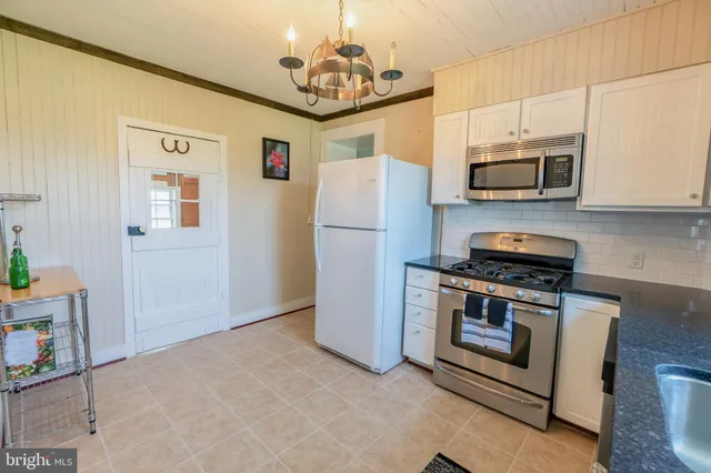 a kitchen with stainless steel appliances granite countertop a refrigerator a stove a microwave oven a sink dishwasher and white cabinets with wooden floor