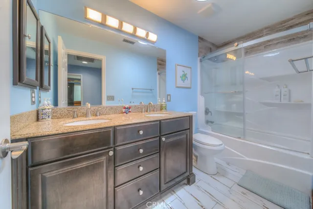 a bathroom with a granite countertop bathtub shower sink vanity and toilet